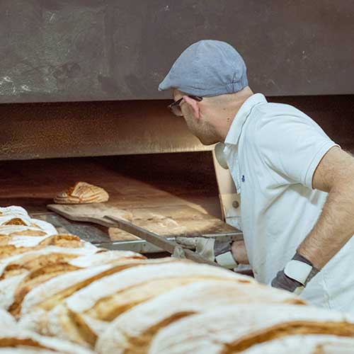 Boulanger enfournant un pain dans un four.